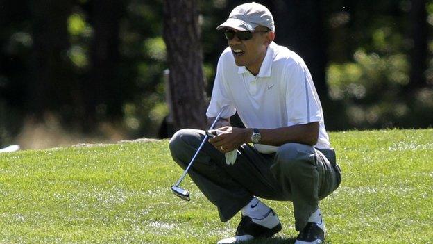 President Barack Obama squats by a golf course green.