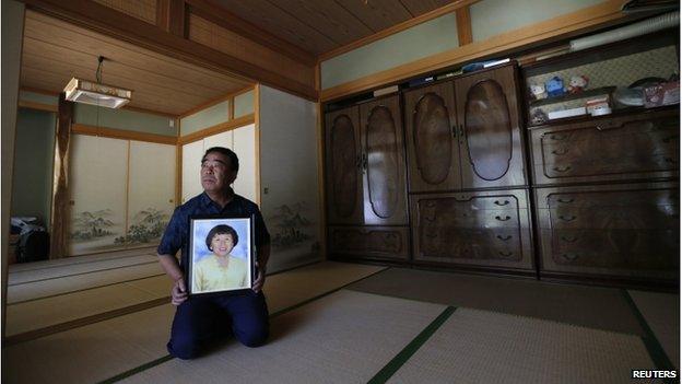 Mikio Watanabe holds a portrait of his late wife Hamako at his home at Yamakiya district in Kawamata town, Fukushima prefecture in this 23 June 2014 file photo