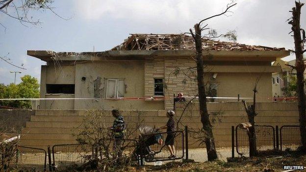 Israelis walk past a house damaged by a rocket in the southern Israeli town of Ashkelon (26 August 2014)