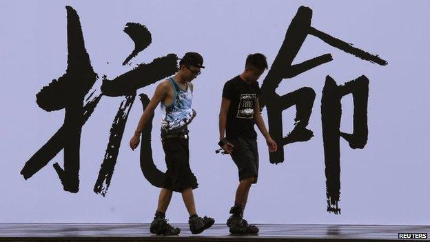 Pro-democracy activists walk past a backdrop with Chinese characters that read "disobedience"