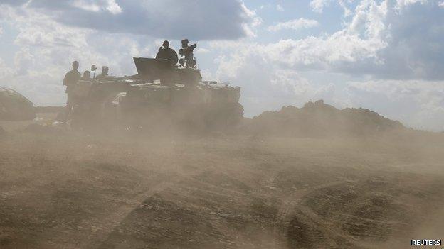 Ukrainian army servicemen around an armoured vehicle are seen through dust raised by passing vehicles near Debaltseve, Donetsk region, on 29 August 2014.