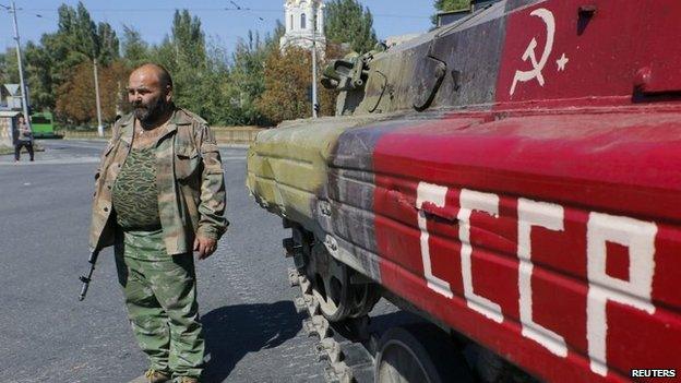 An armed pro-Russian separatist stands next to an APC in the city of Donetsk