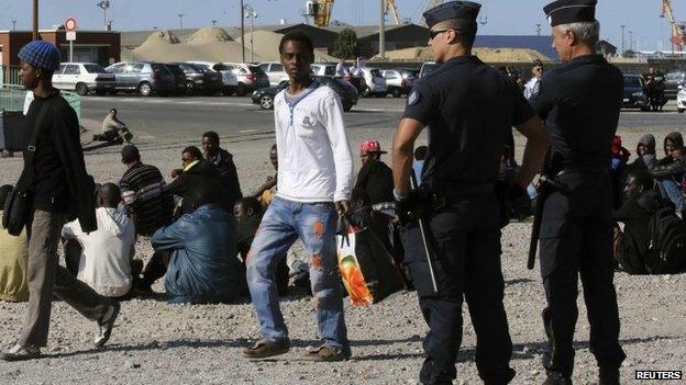 French riot police stand guard as migrants wait to receive a daily food handout near the city hall in Calais (5 August 2014)