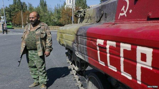 An armed pro-Russian separatist stands next to an APC in the city of Donetsk