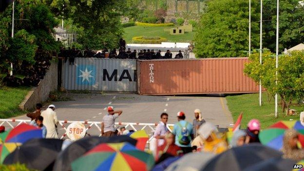 Pakistan riot policemen sit on top of shipping containers, used as roadblocks leading to Prime Minister House