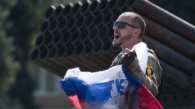 A pro-Russian rebel holds a Russian national flag near to damaged heavy hardware from the Ukrainian army during an exhibition in the central square in Donetsk, eastern Ukraine, Sunday, Aug. 24