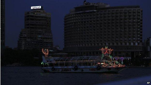 A boat sails along the Nile river as the Garden city neighbourhood, background, remains in darkness during a power cut, Cairo, Egypt, 5 September 2014