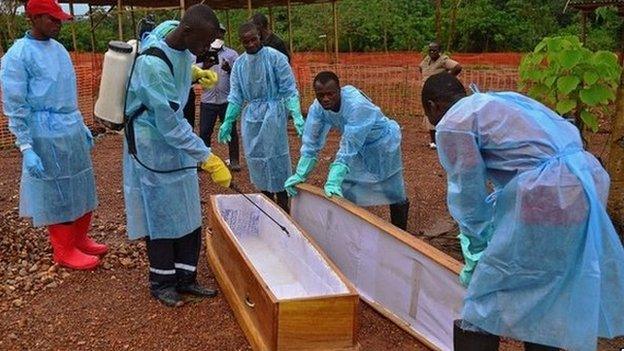 Sierra Leone government burial team members wearing protective clothing disinfect a coffin at a MSF facility, 14 August