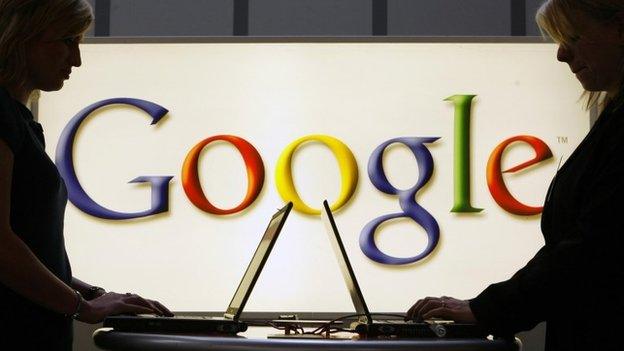 Google logo in background of two people on laptops