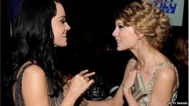 Katy and Taylor smiling together as they chat with swift's arm on Katy