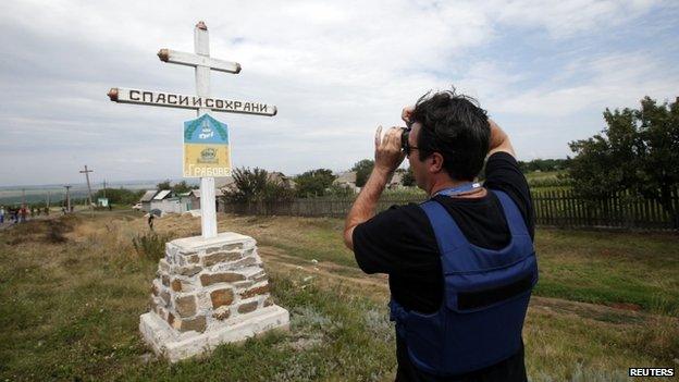 An Organisation for Security and Cooperation in Europe (OSCE) monitor photographs the village sign at the crash site of Malaysia Airlines Flight MH17, near the settlement of Grabovo in the Donetsk region