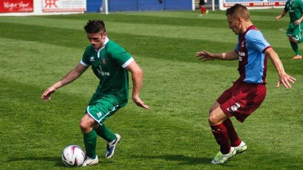 Liam in green kit with ball, opponent next to him