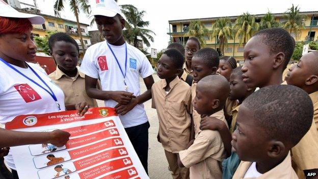 Volunteers wearing t-shirts of the United Nations Development Programme (UNDP) show a placard to raise awareness on the symptoms of the Ebola in Abidjan, Ivory Coast (15 September 2014)