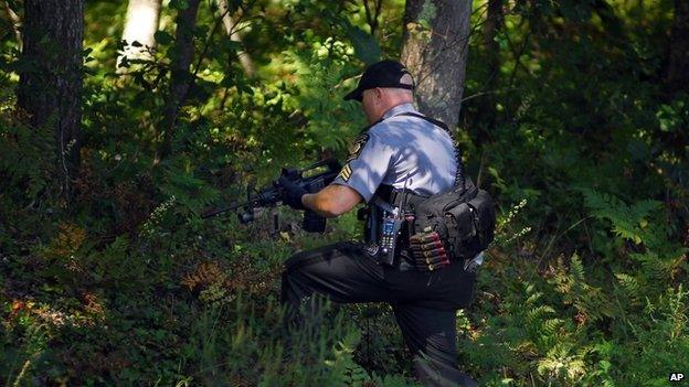 A Pennsylvania State Trooper walks into a wooded area as investigators return to scour the woods across the street from the state police barracks