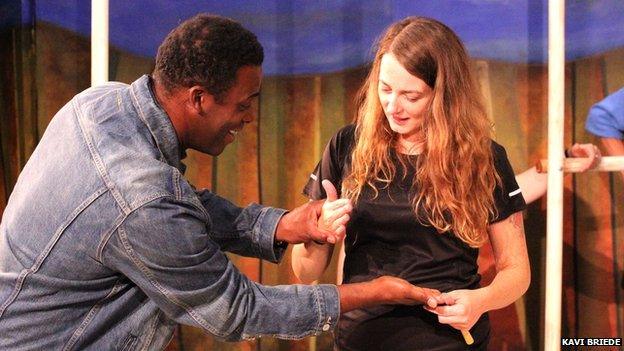 Sophie and a male actor during rehearsal. He is holding both her hands and leaning in towards her.