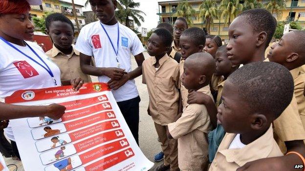 Volunteers wearing United Nations Development Programme (UNDP) T-shirts show a placard to raise awareness about the symptoms of the Ebola virus to students of the Sainte Therese school, in the Koumassi district, in Abidjan, Ivory Coast - 15 September 2014