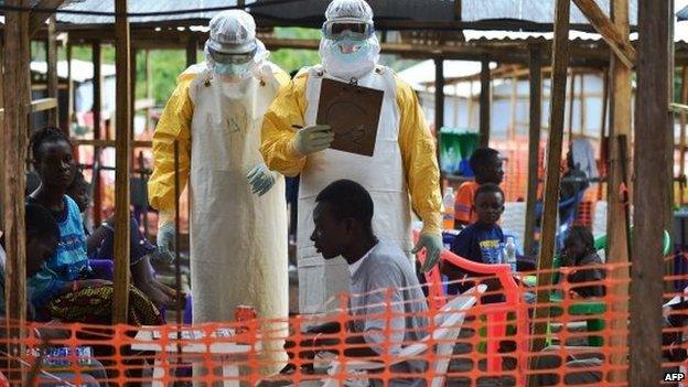 An MSF medical worker, wearing protective clothing, relays patient details and updates behind a barrier to a colleague at an MSF facility in Kailahun in Sierra Leone on 15 August 2014