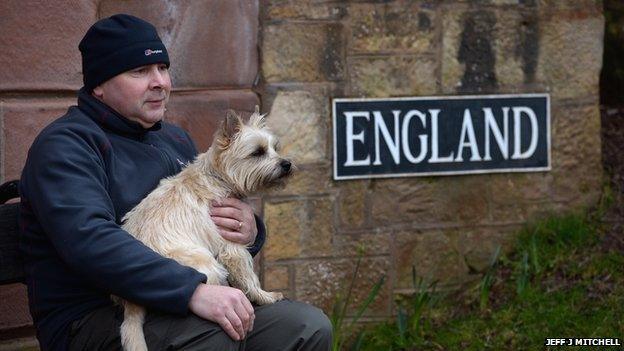 A man and a dog sit next to a sign saying "England"