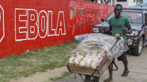 Vendor pushes bread past sign warning of Ebola risks