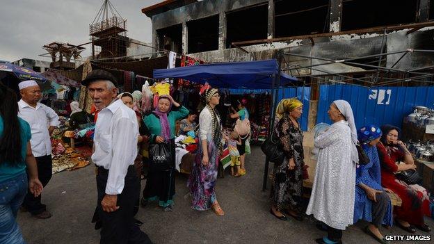 Uighur traders beside a burnt out market building at the main bazaar in Turpan, Xinjiang region, on 27 June 2013