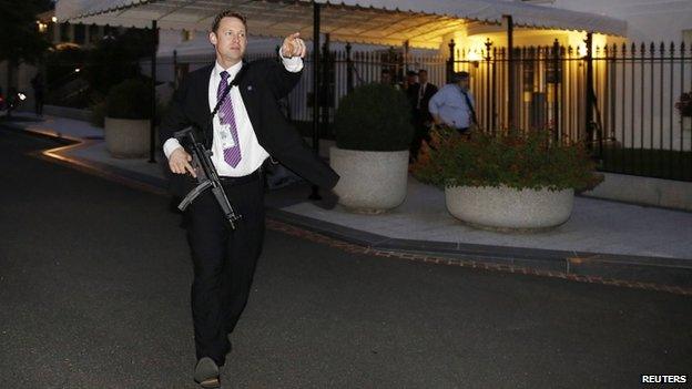 A US Secret Service agent with an automatic rifle hurries people to evacuate the White House complex over a security alert