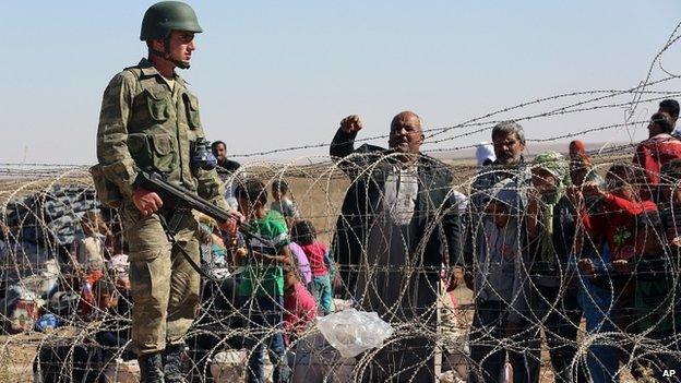 Turkish soldier stands guard as Syrian refugees wait to cross border in Suruc, Turkey. 21 Sept 2014