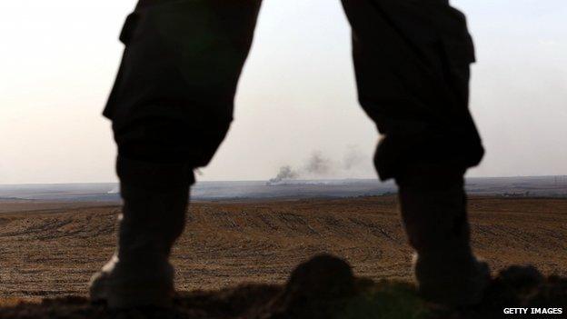 An Iraqi Kurdish Peshmerga fighter holds a position as smoke billows on the front line in Khazer, 40 km West of Irbil, in northern Iraq on 16 September 2014.