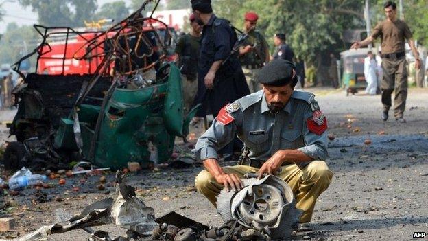 Pakistani police officials examine mangled wreckage at the site of a suicide bomb attack in Peshawar on September 23, 2014.