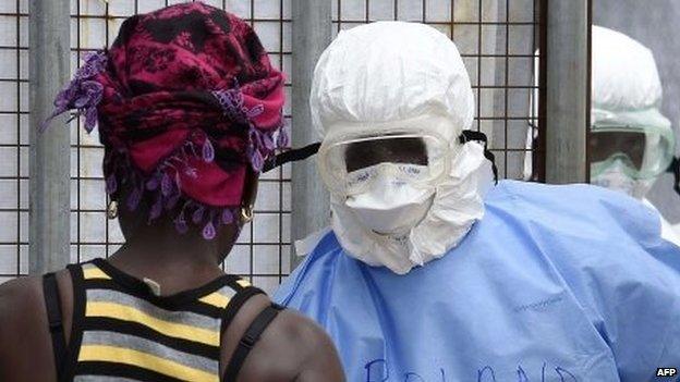 Health workers in protective suits greet a woman who has come to deliver food to relatives at Island Hospital where people suffering from the Ebola virus are being treated in Monrovia on 30 September 2014