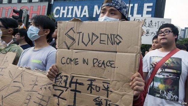 Protesters hold signs reading "students come in peace", outside the venue of the China National Day flag-raising in Hong Kong on 1 Oct.