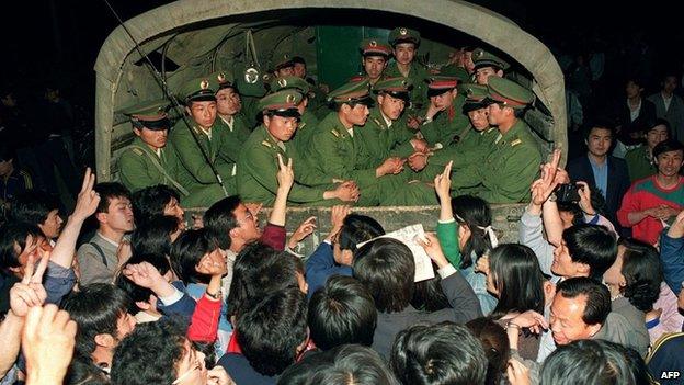 Pro-democracy demonstrators raise their fists and flash "victory" signs as they stop a military truck filled with soldiers on its way to Tiananmen Square