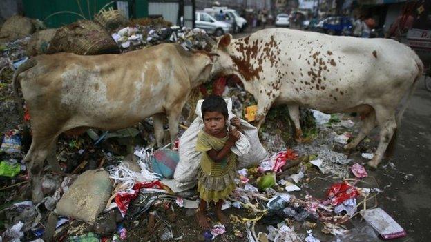 A homeless child rag picker waits to cross a road after collecting recyclable material from a garbage dump in Gauhati, India, Sunday, Sept. 28, 2014.