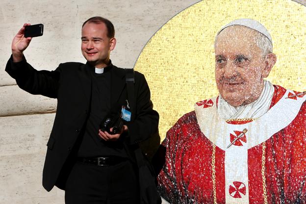 Priest takes selfie in front of image of Pope Francis