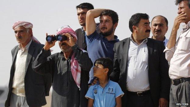 Turkish and Syrian Kurds stand on a hill near Kobane to watch the battle with IS militants (3 October 2014)