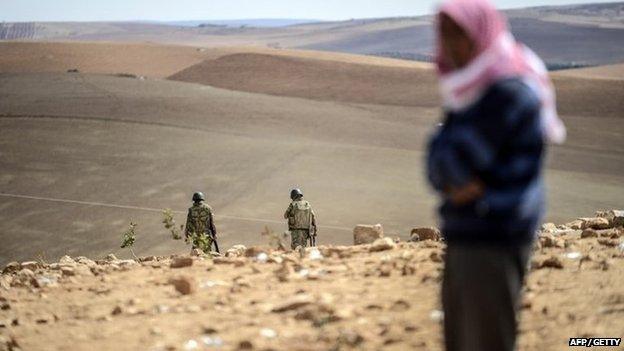 A Syrian Kurd stands as Turkish soldiers patrol near the Syrian border around Suruc on 30 September 2014.