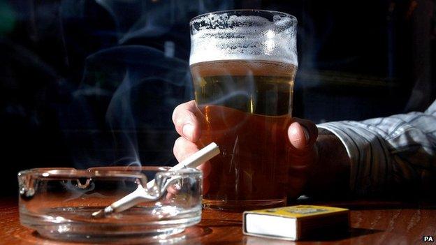 Man holding pint of beer and lit cigarette in ashtray