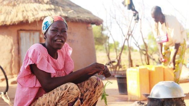 Woman sitting in front of traditional house, with man in the background