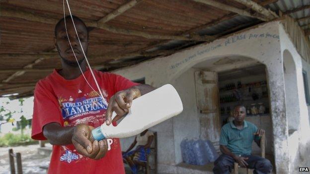 A Liberian man washes his hands from a water bottle tied to a roof outside a shop to curb the spread of Ebola in Dolos Town Community, Margibi County (9 October 2014)