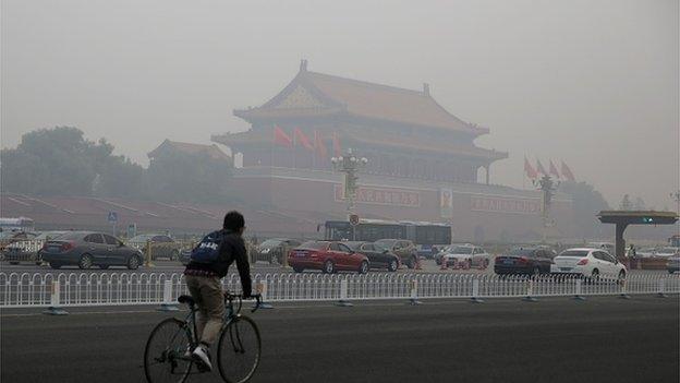 A cyclist rides past the Tiananmen Rostrum as heavy smog engulfs the city