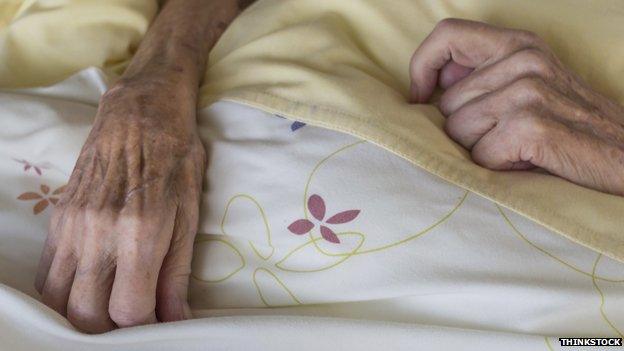 Old and thin hands on a bed