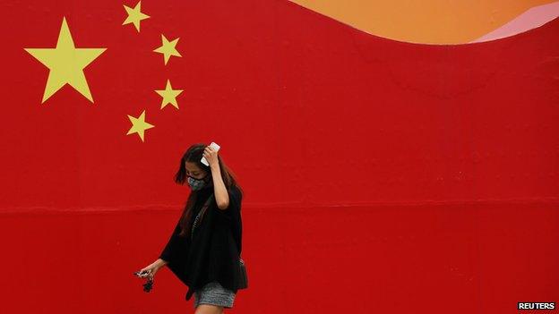 Woman in a mask walks past Chinese flag mural, Beijing (10 Oct)