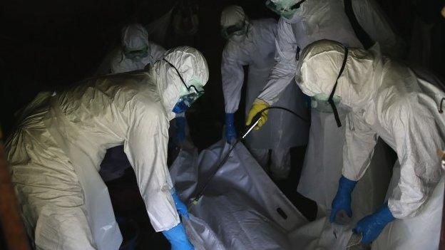 A burial team from the Liberian Red Cross sprays disinfectant over the body bag of an Ebola victim while collecting the man his home on 8 October 2014 near Monrovia, Liberia