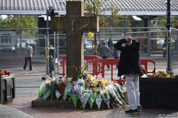 A man observes the floral tributes at the base of the Eccles Cross