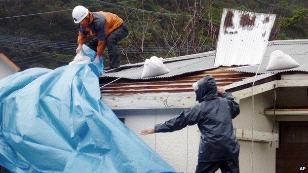 People try to repair a roof damaged by heavy wind and rain as typhoon Vongfong approaches in Amami, Kagoshima, 12 October 2014