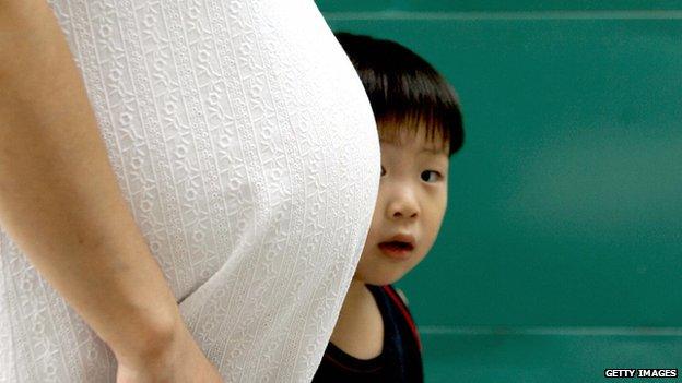 a South Korean child stares behind a belly of his pregnant mother