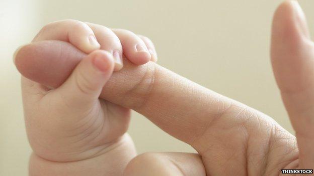 A baby holds an adult's finger