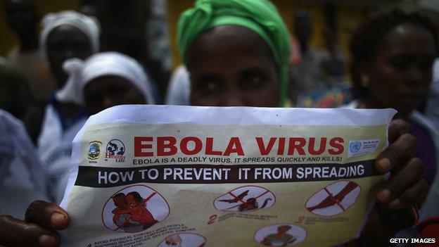 Woman holding up Ebola information poster