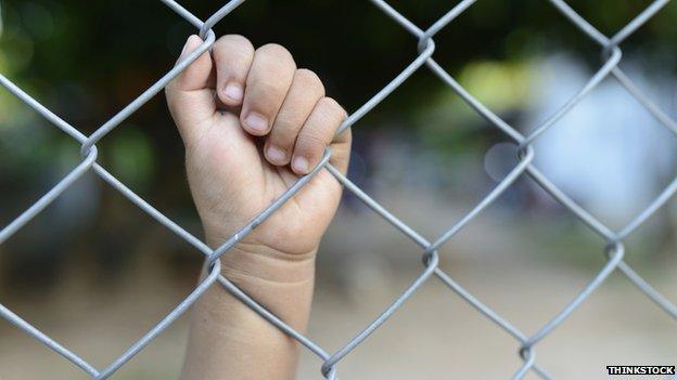 Child's hand on prison fence