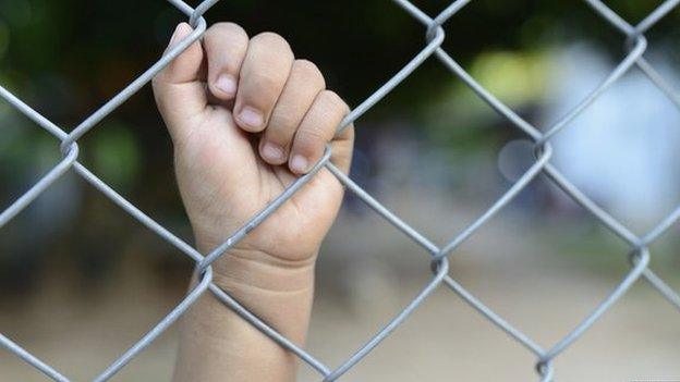 Child's hand on prison fence