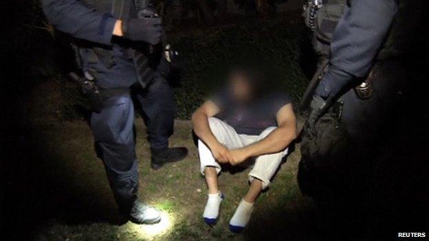 A man detained during a raid sits on the ground between police officers in Sydney, in this still image taken from a police handout video on 18 September, 2014